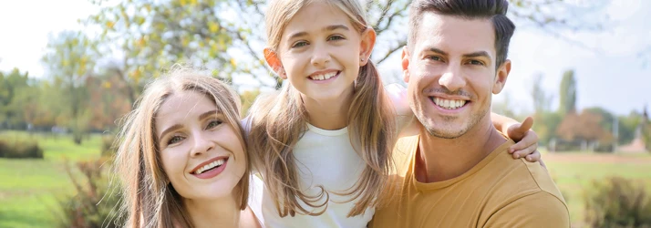 Dentist Winslow ME Family Dentistry Focused family of three is outside at a park embracing while posing for the camera